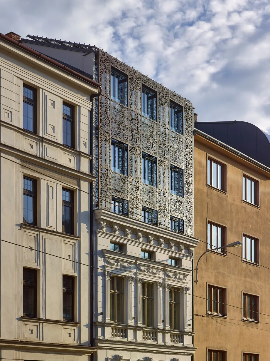 Building with classical lower facade and modern upper facade featuring intricate metalwork panels.