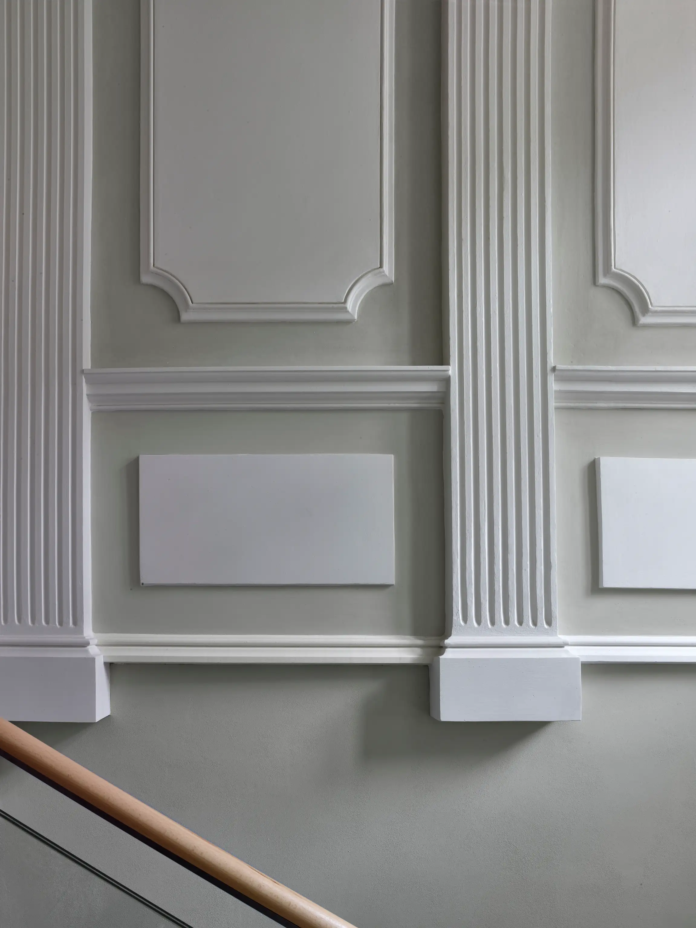 Ornate white molding on gray wall with a wooden handrail in the lower left corner.