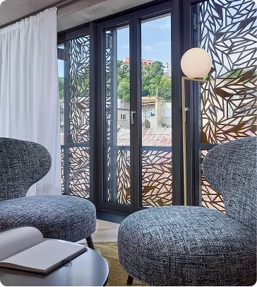 Modern living room with patterned glass doors, two grey chairs, floor lamp, and city view outside.