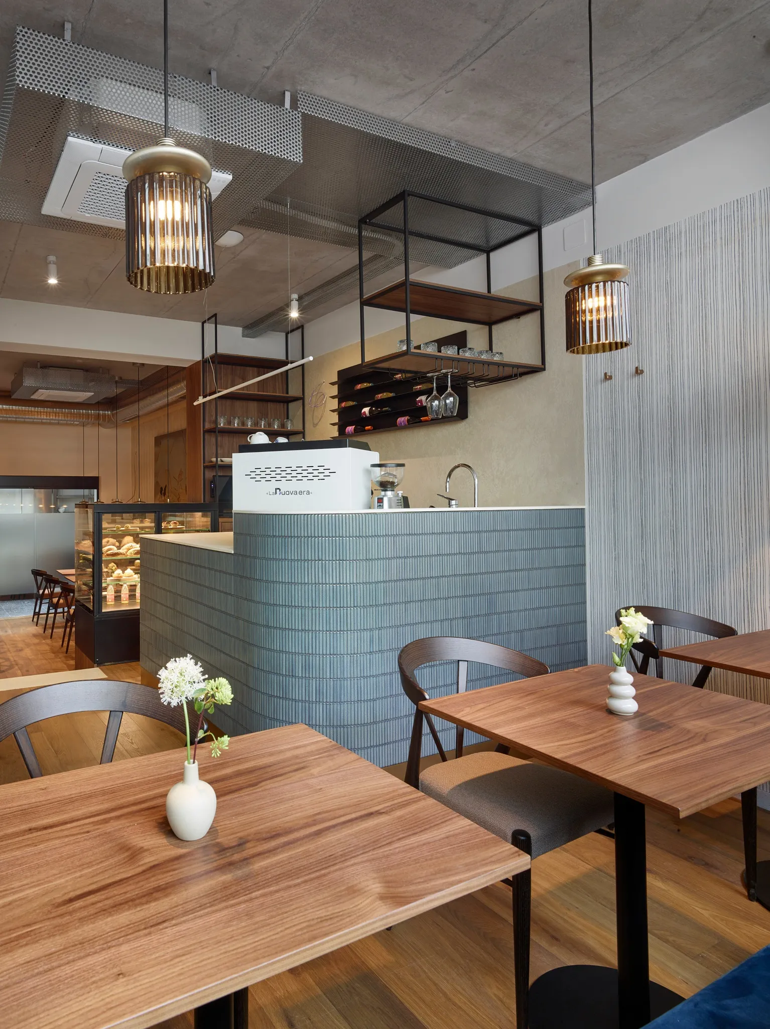 Modern café interior with a coffee counter, hanging shelves, wooden tables, and pendant lights.