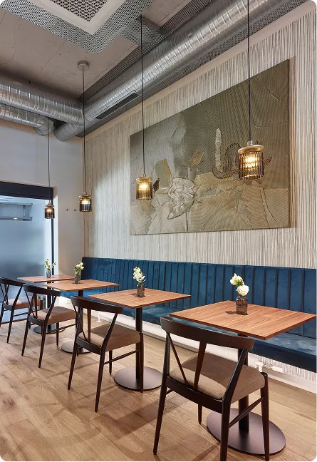 Modern cafe interior with wooden tables, blue bench seating, pendant lights, and floral centerpieces.