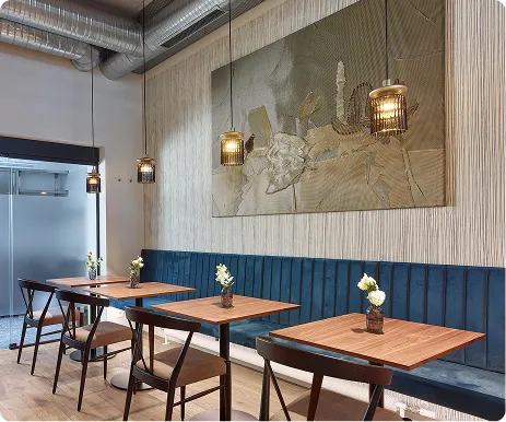 Modern café interior with wooden tables, blue bench seating, hanging lamps, and wall art.