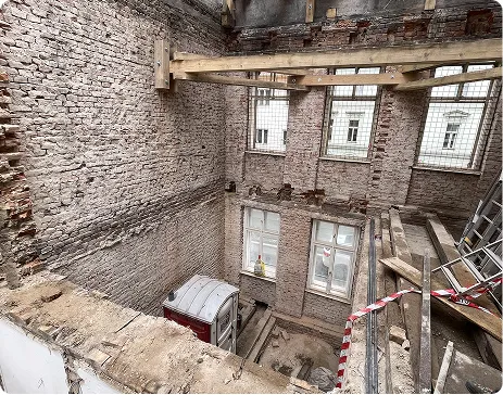 Interiér rozebrané budovy s odkrytou cihlovou zdí a staveništní lávkou u oken.