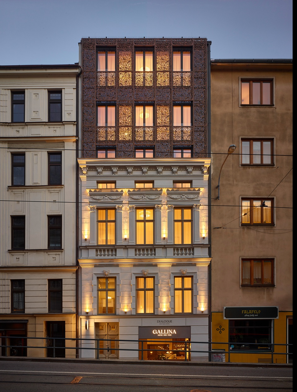 Osvětlená historická budova s vyřezávanou moderní fasádou v horní části a kavárnou Gallina v přízemí.