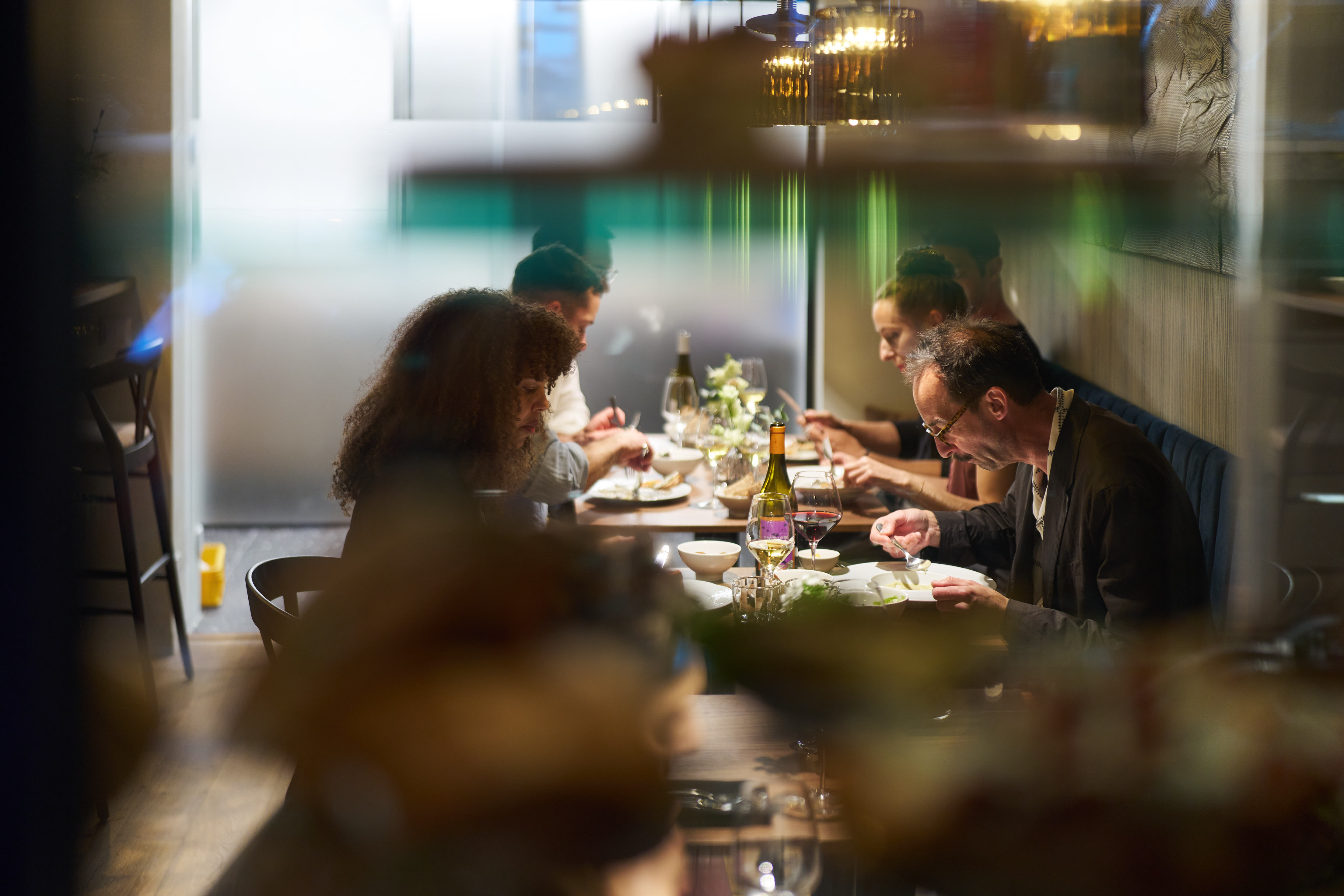 Skupina lidí si v útulné restauraci užívá společnou večeři u stolu s víny a pokrmy.