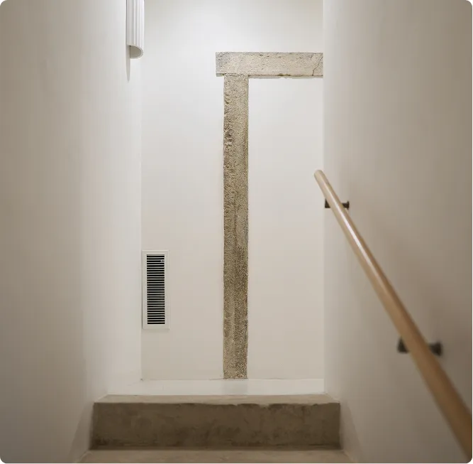 Úzké schodiště se dvěma schody, kovovým madlem vpravo a kamenným obložením na zdi.