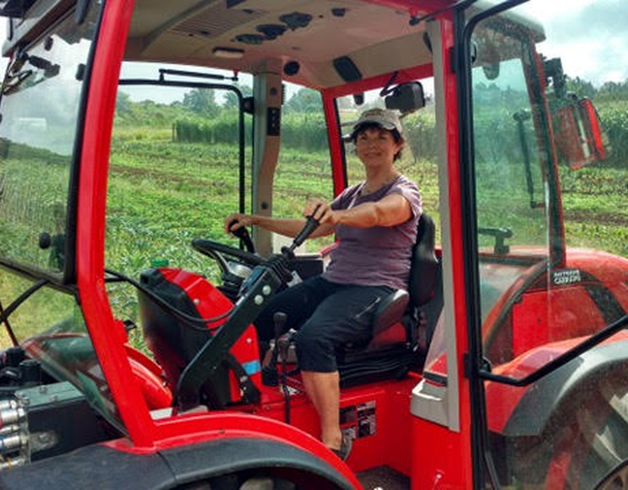 Woman wearing a cap sitting and operating a red tractor in a green field.