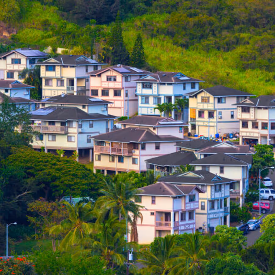 Cluster of multi-story residential houses surrounded by lush greenery and palm trees on a hillside.
