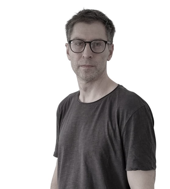 Man with glasses and short hair wearing a dark t-shirt looking straight ahead.