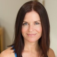 Smiling woman with straight brown hair and blue eyes in a softly lit indoor setting.