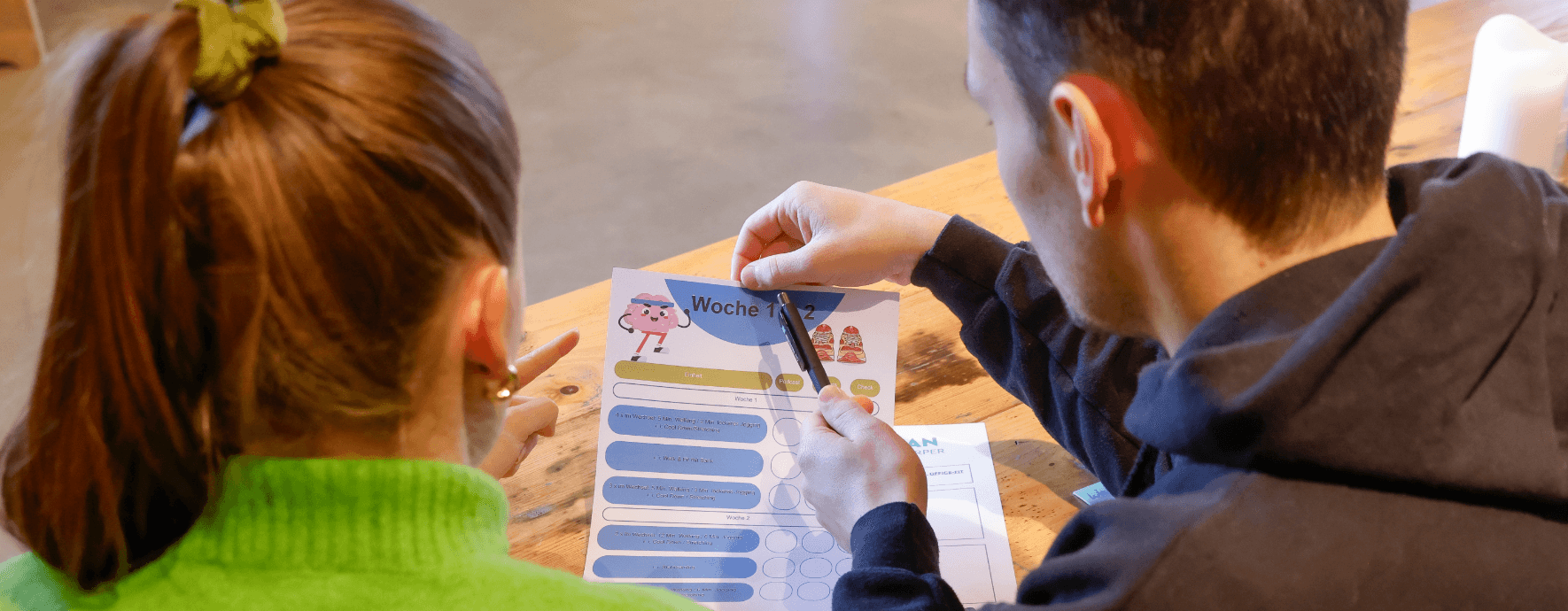 Zwei Personen vor einem Ablaufplan eines Workshops am Tisch sitzend