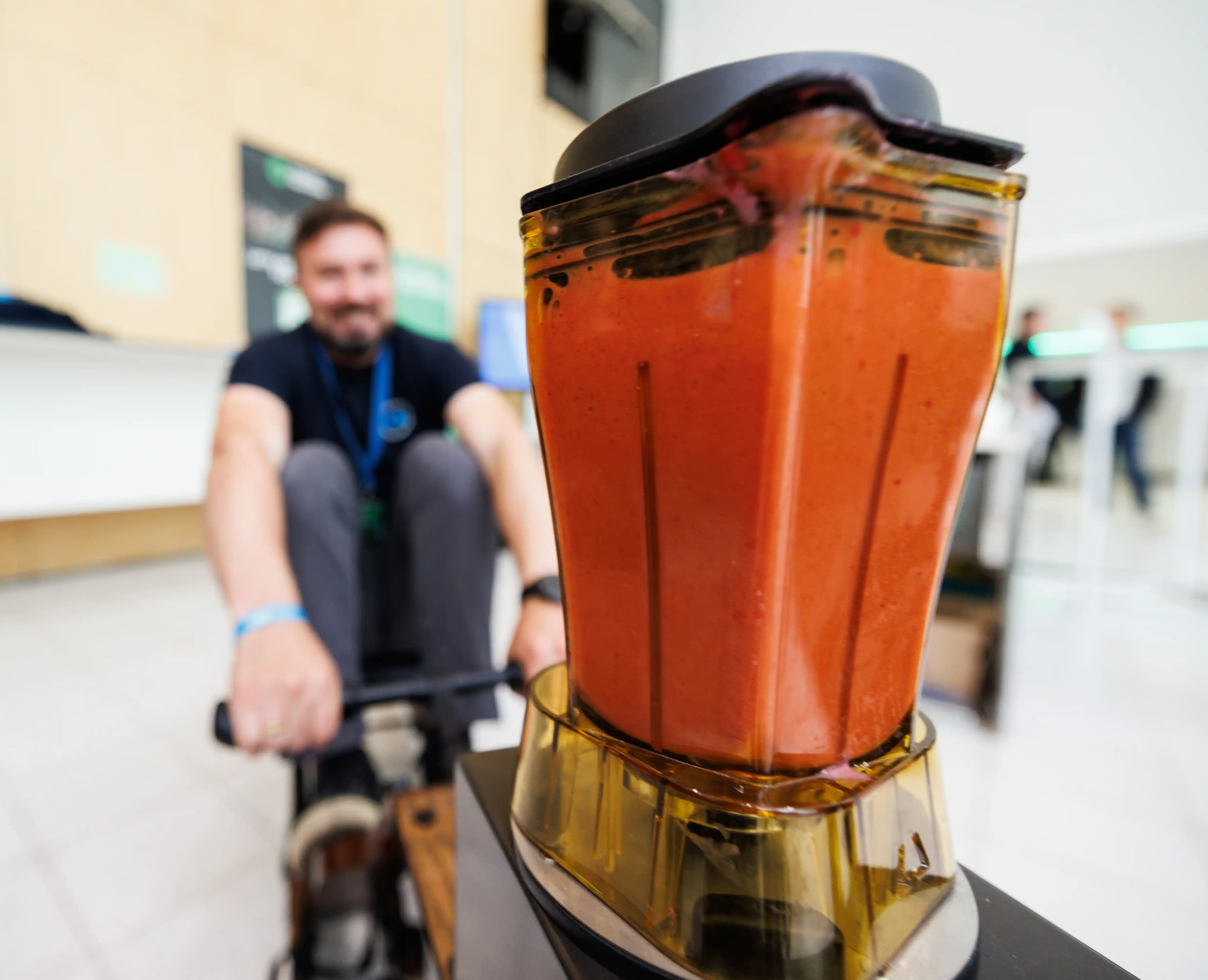 Ein Mann sitzt auf dem Smoothie Rower und im Vordergrund ist der Smoothie Mixer mit roter Flüssgkeit zu sehen