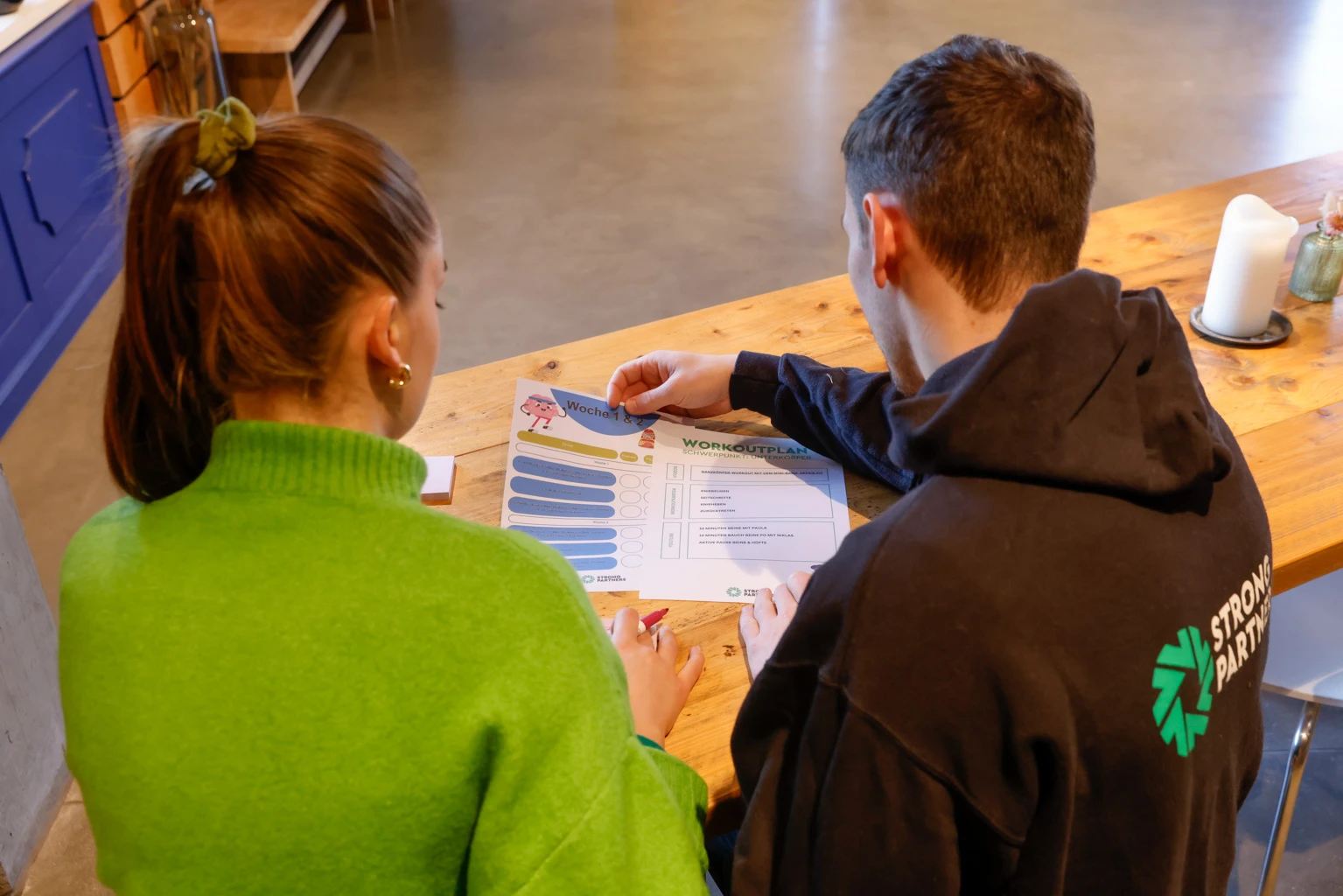 Zwei junge Menschen sitzen an einem Tisch vor einem Plan und arbeiten daran