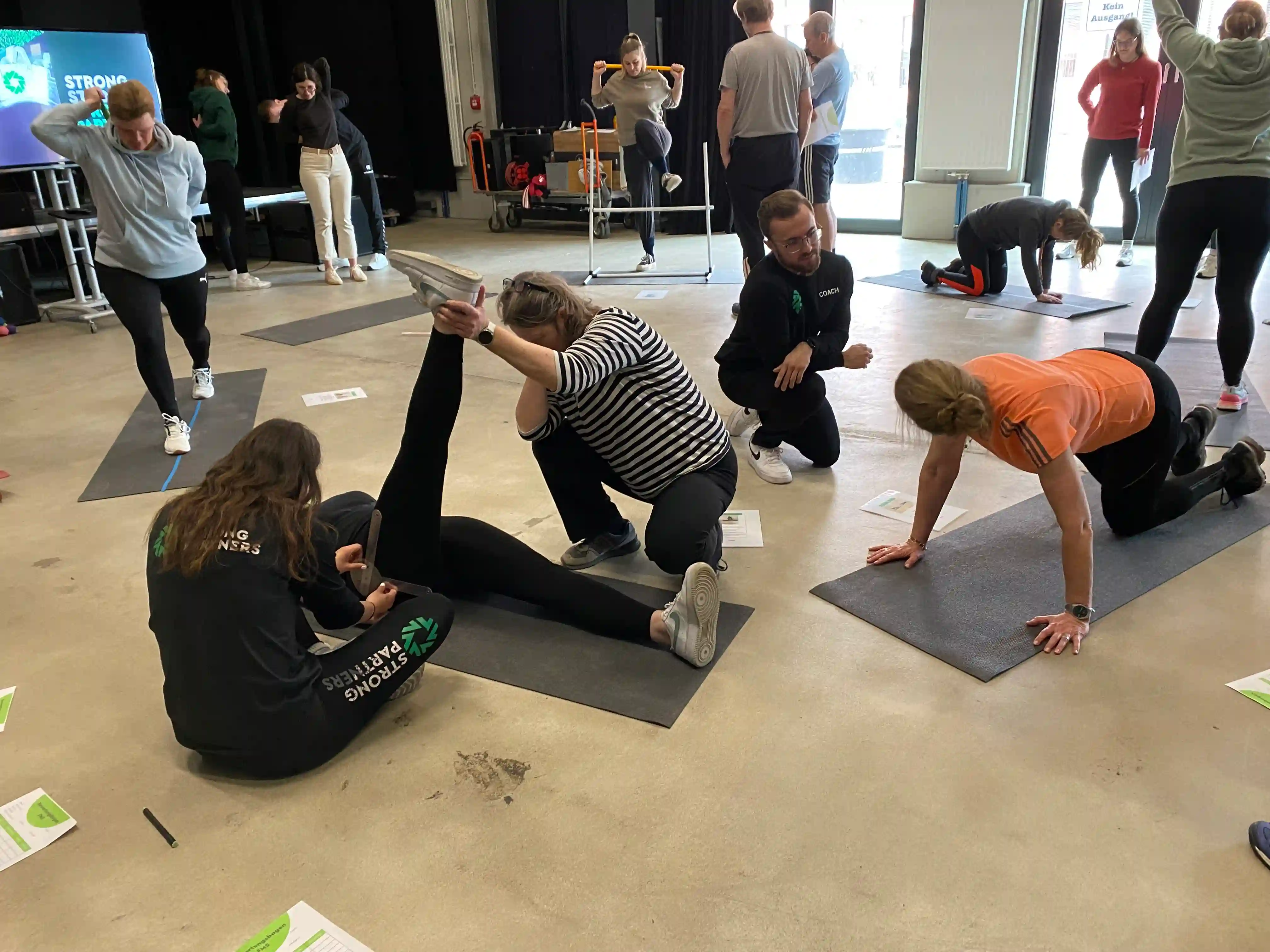 Trainer prüft die Haltung eines Teilnehmers bei einer Arm- und Beinübung im funktionellen Bewegungstest