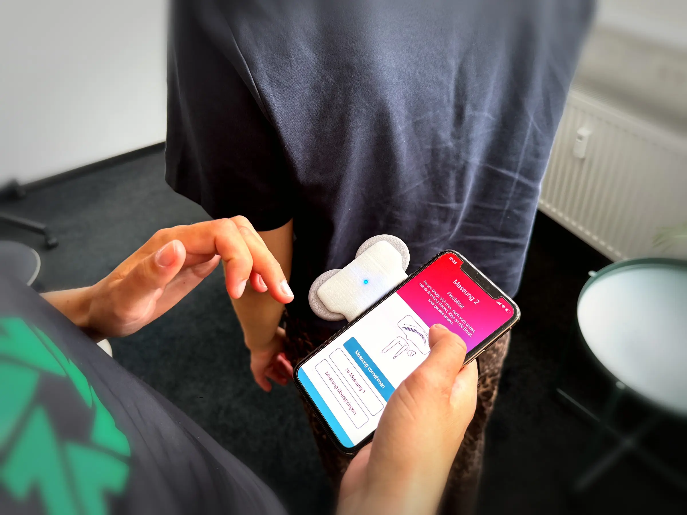 Smartphone mit Strong-Partners-App zeigt den Messschritt „Flexibilität" der Wirbelsäulenmessung, aufgesetzter Messsensor.