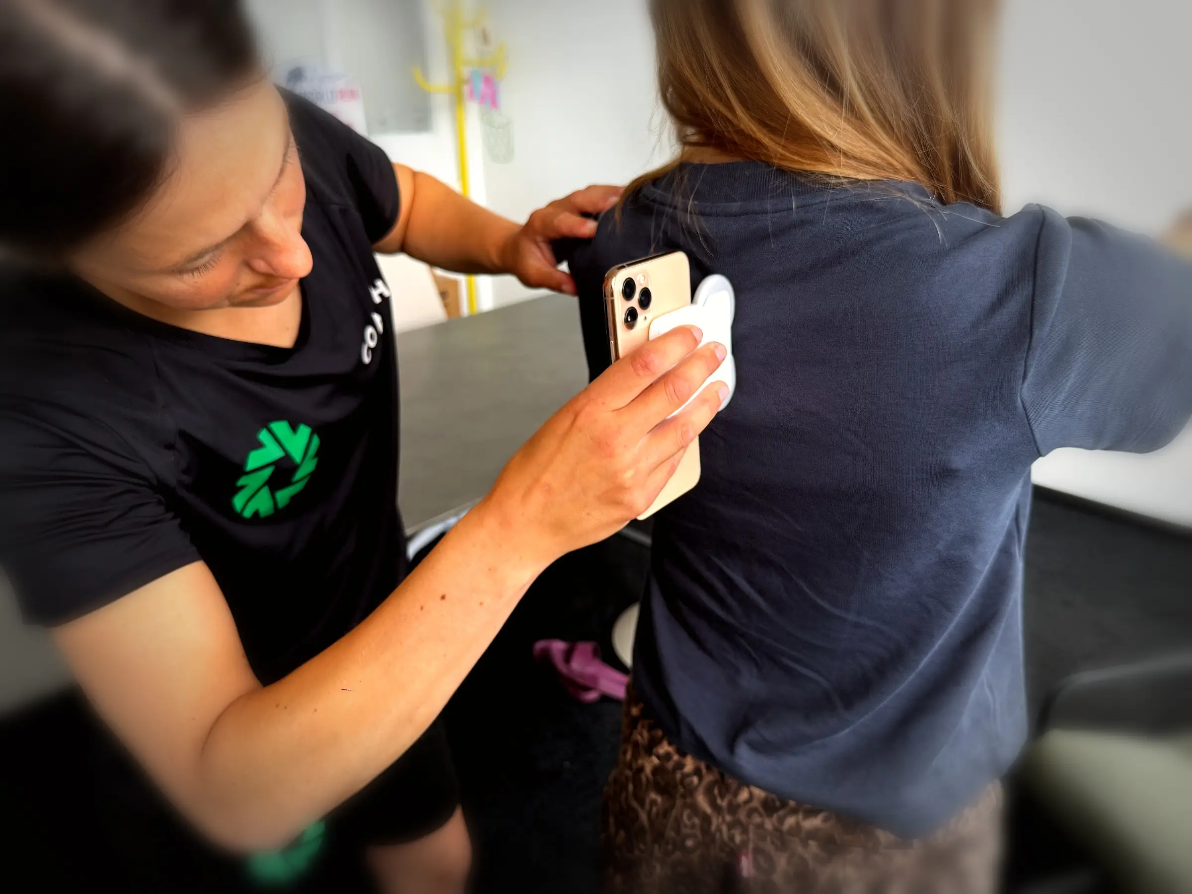 Strong-Partners-Trainerin setzt den Messsensor mit dem Smartphone am oberen Rücken einer Kollegin an.