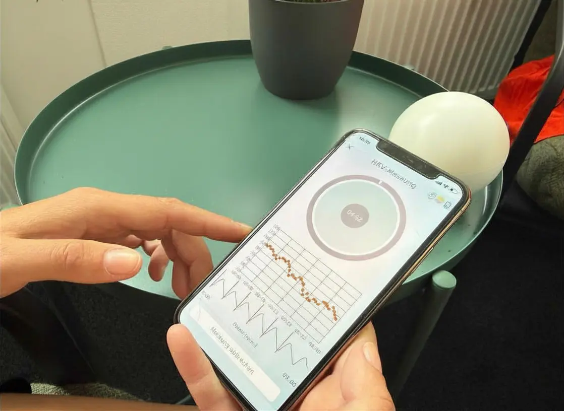 Laufende HRV-Messung mit Pulskurve auf dem Smartphone, Sensorkugel auf dem Beistelltisch.