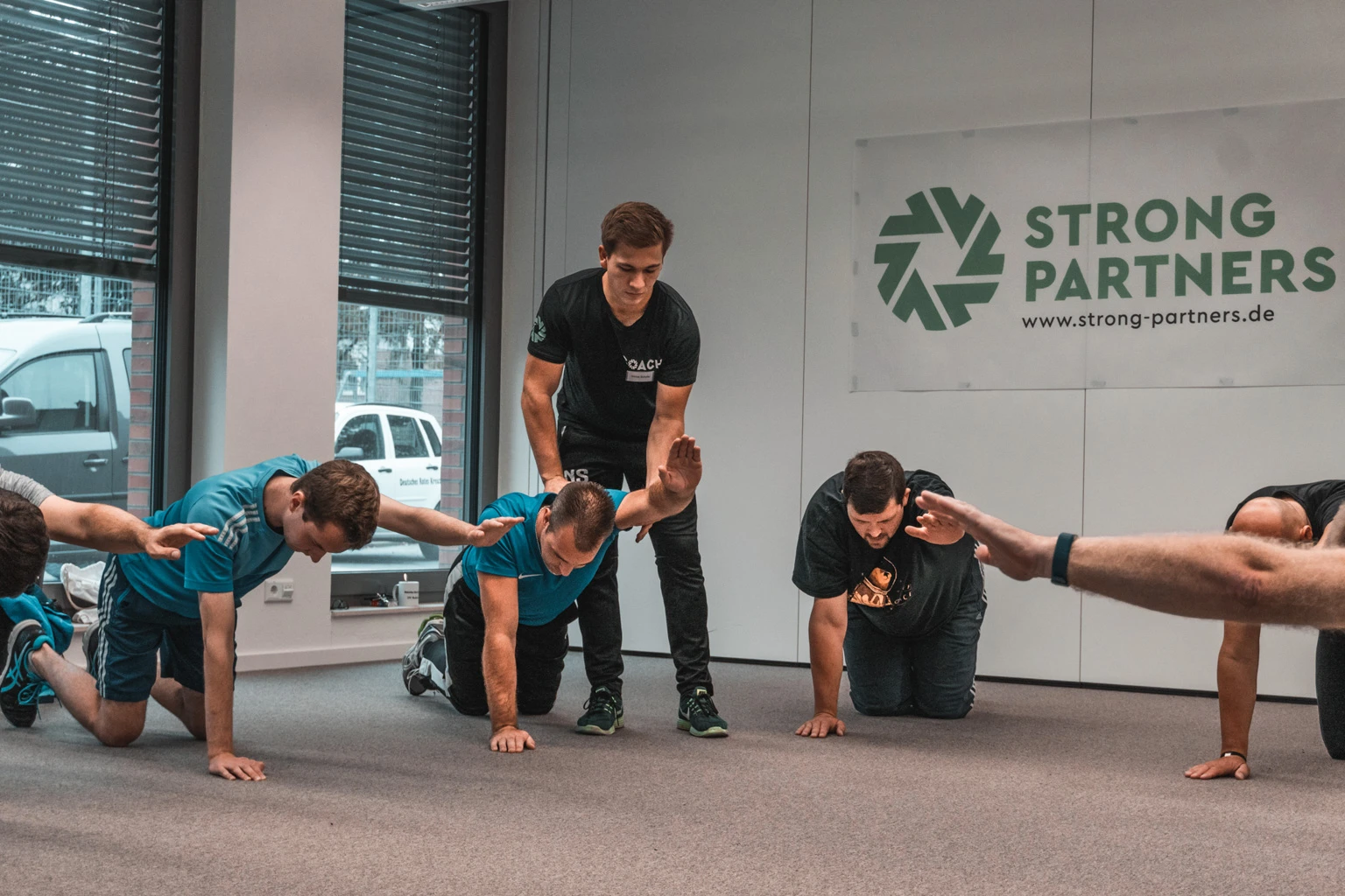 Teilnehmende eines Rückenfit Kurses werden von einem Strong Partners Coach in der Übung korrigiert