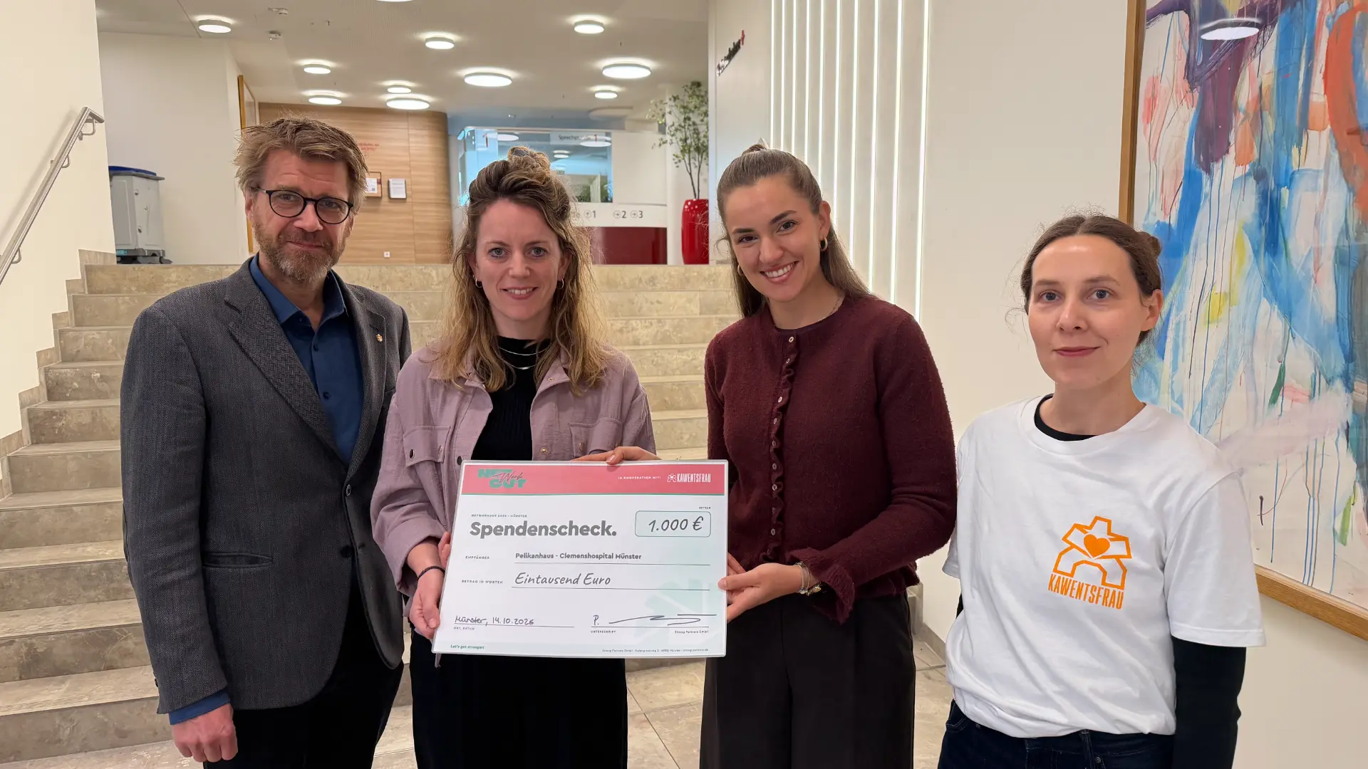 Vier Personen halten im Foyer des Clemenshospitals Münster einen Networkout-Spendenscheck über 1.000 Euro für die Initiative Kawentsfrau