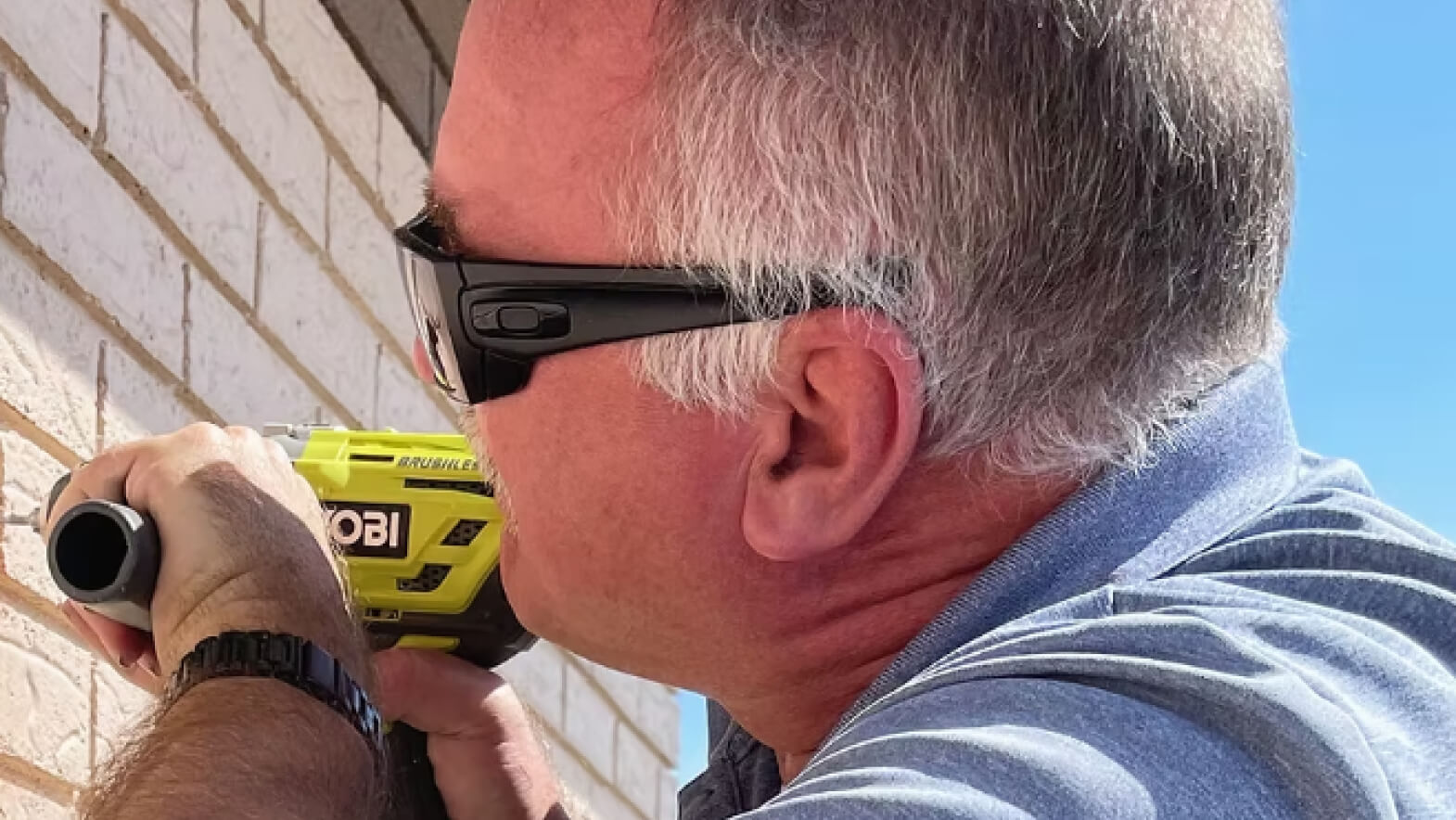 Close-up of an installer drilling into a brick wall to mount graphics