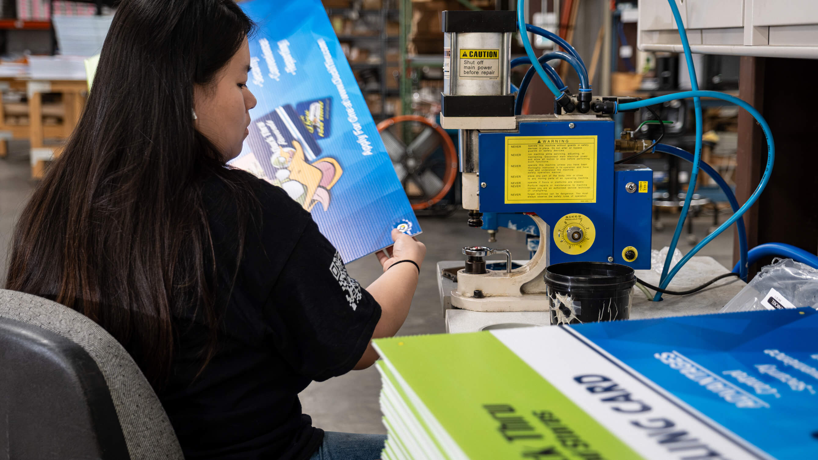A production worker assembling printed rewards cards at a riveting station