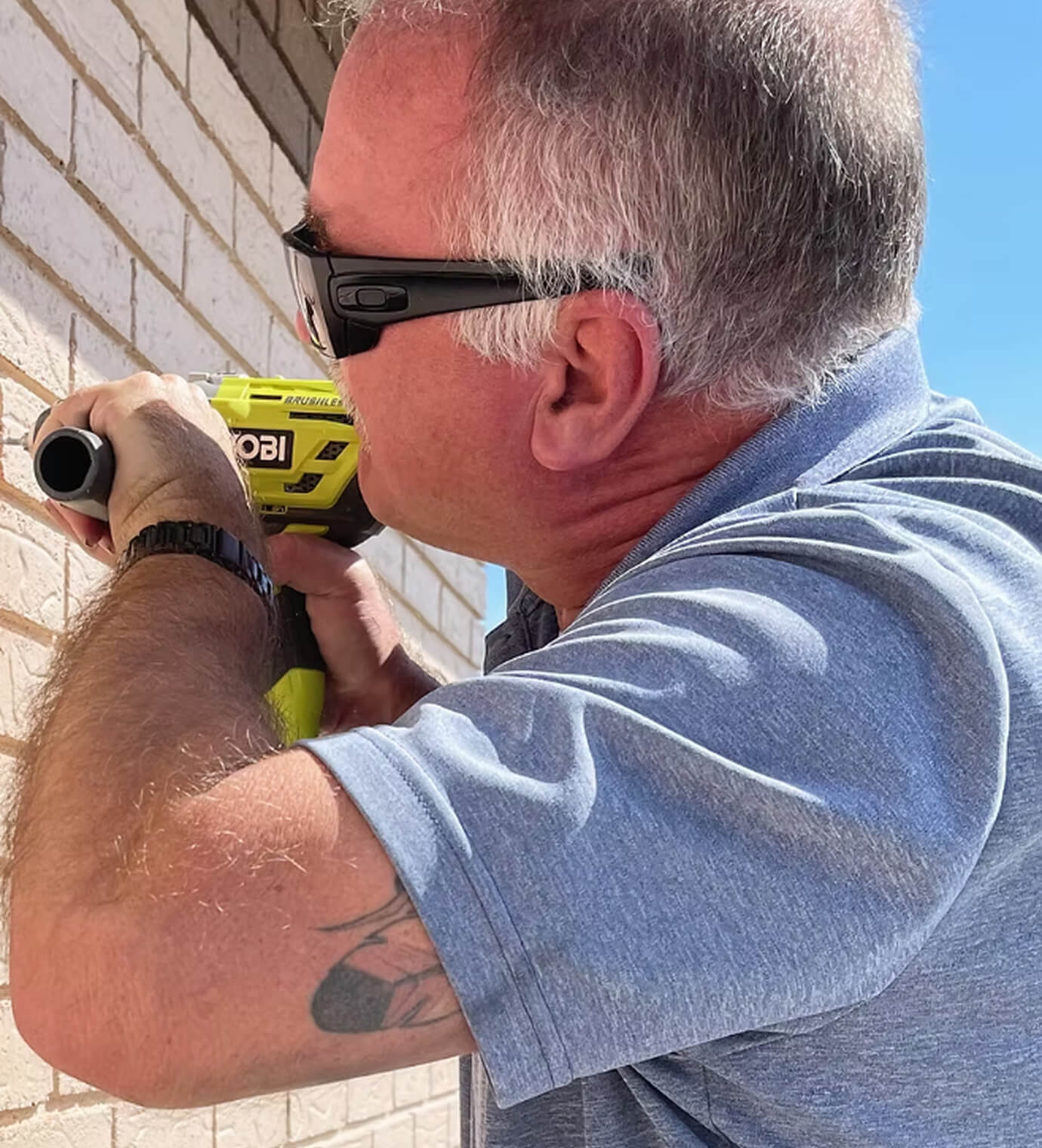 A TEC Graphics installer mounting signage to an exterior brick wall with a power drill