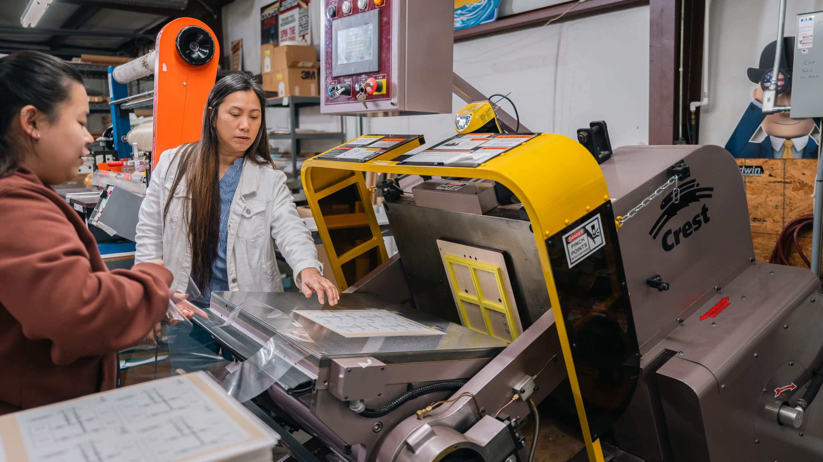 Two workers running a printed sheet through a Crest die-cutting machine