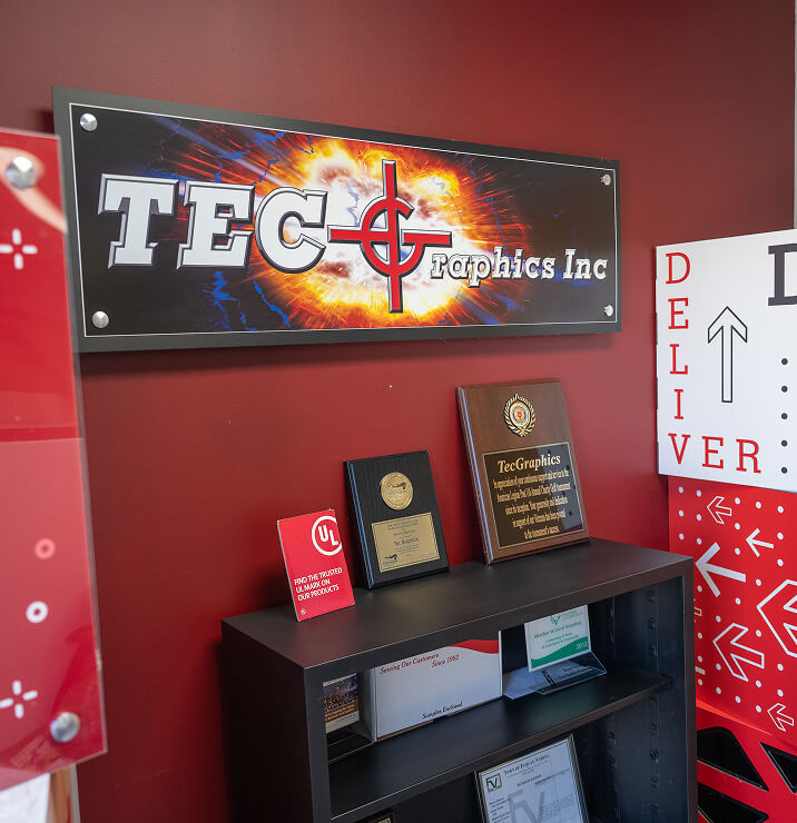 A backlit TEC Graphics Inc logo sign above an award shelf in the lobby