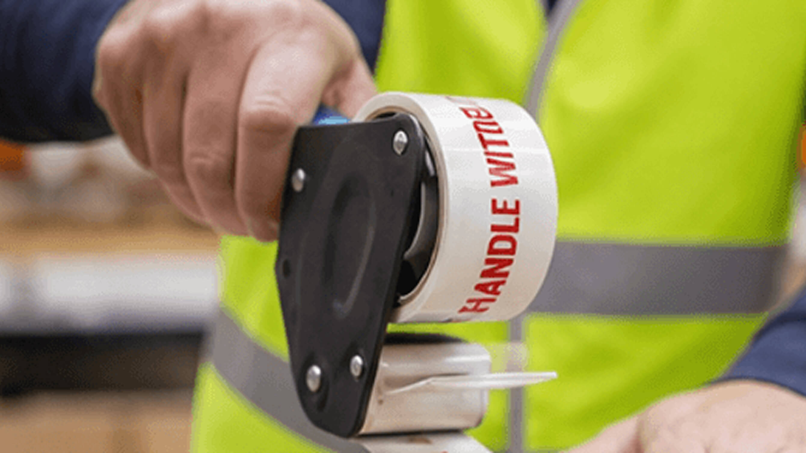 A worker in a hi-vis vest applying printed Handle With Care packing tape to a shipment