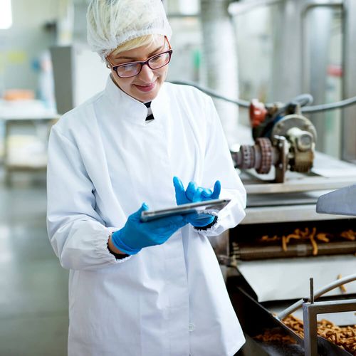 A food-manufacturing worker with a tablet beside a pretzel production line