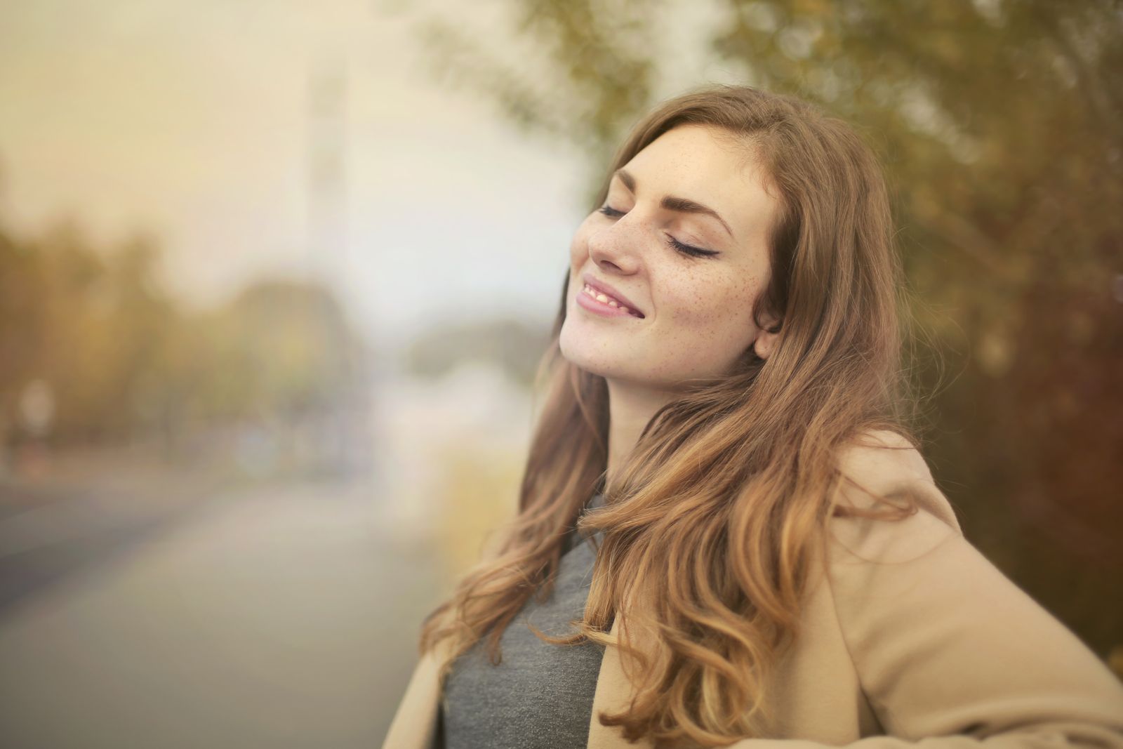 Woman with closed eyes smiling peacefully outdoors in soft autumn light