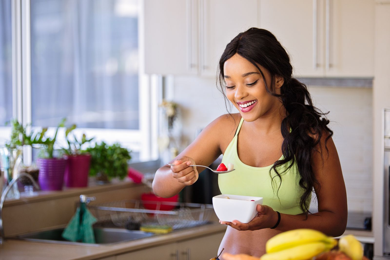 Smiling woman enjoying a fruit bowl in a bright kitchen