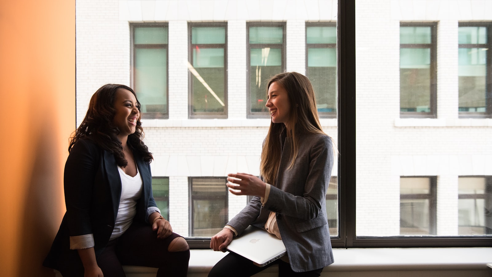 Two women sitting by a window, talking and laughing