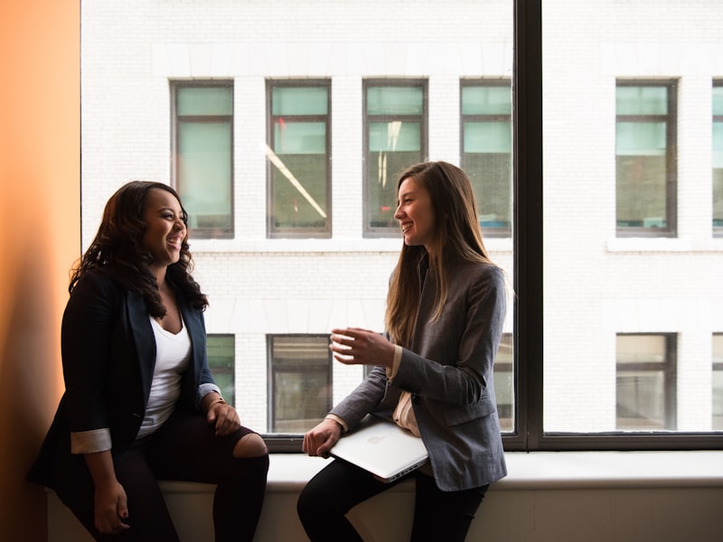 Two women sitting by a window, talking and laughing