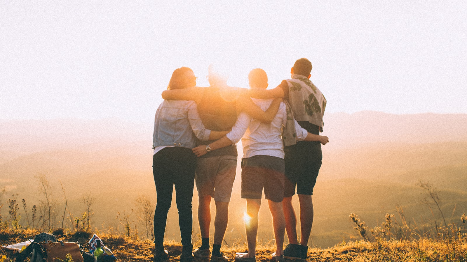 Four friends standing arm in arm on a hilltop at sunset
