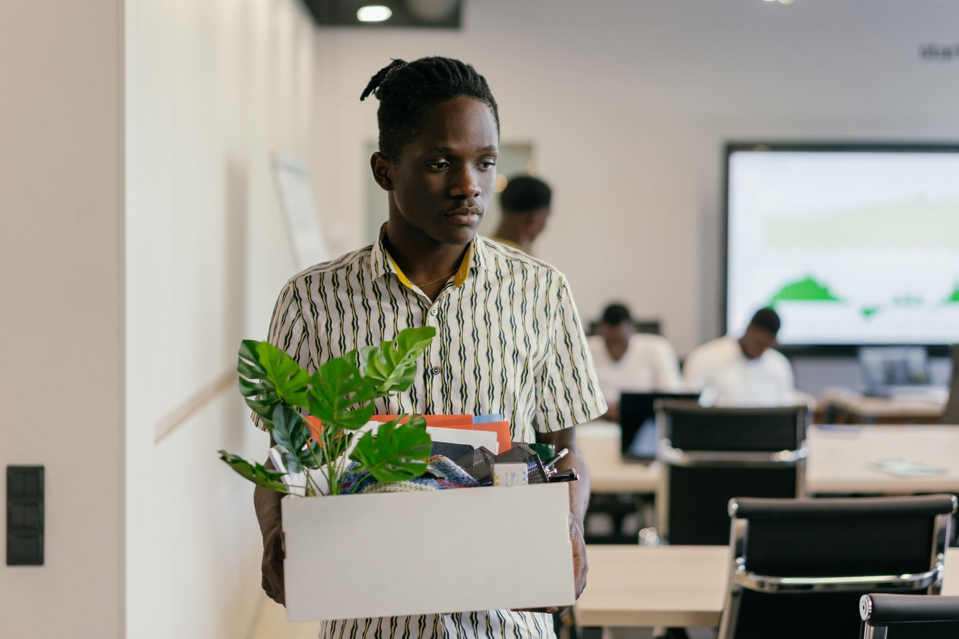 A man carrying a box with a plant and folders out of an office