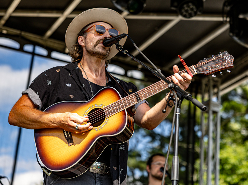 Guitarist in a wide-brimmed hat and sunglasses singing and playing an acoustic guitar