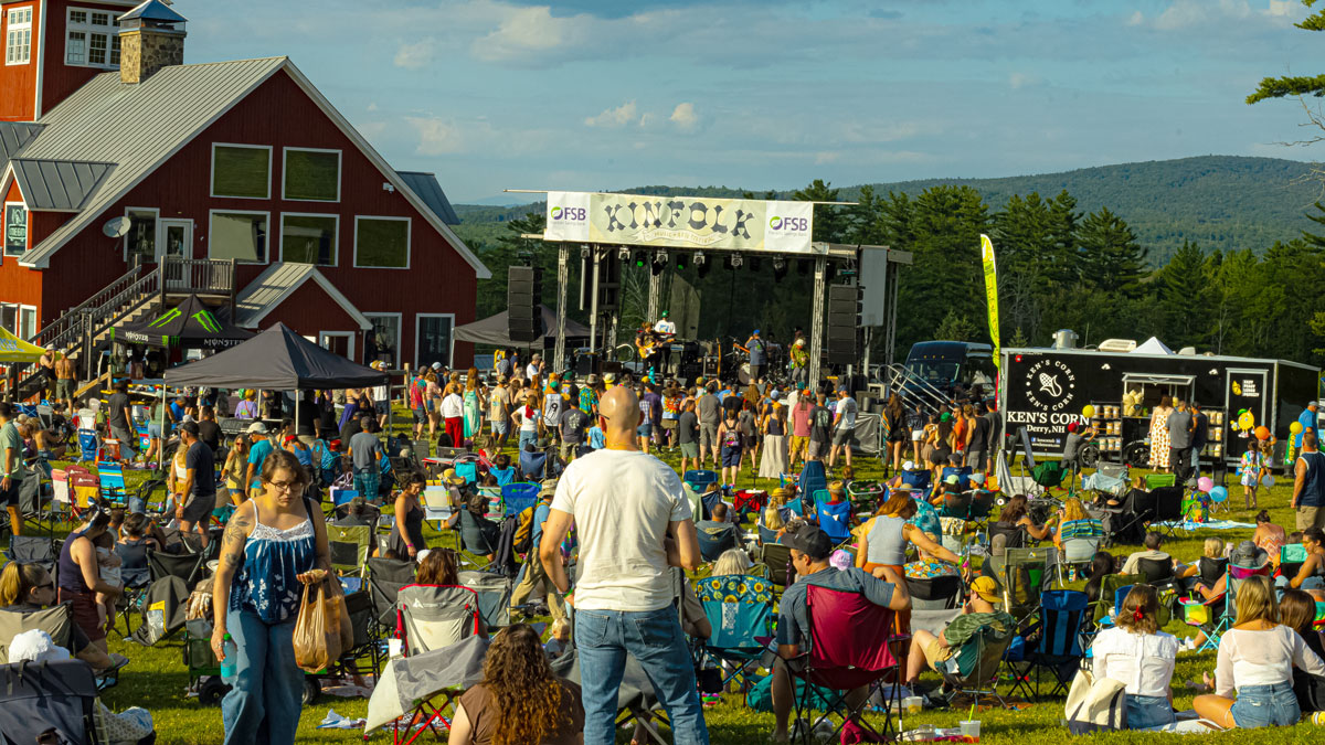 Crowd relaxing in lawn chairs in front of the Kinfolk stage beside a red barn