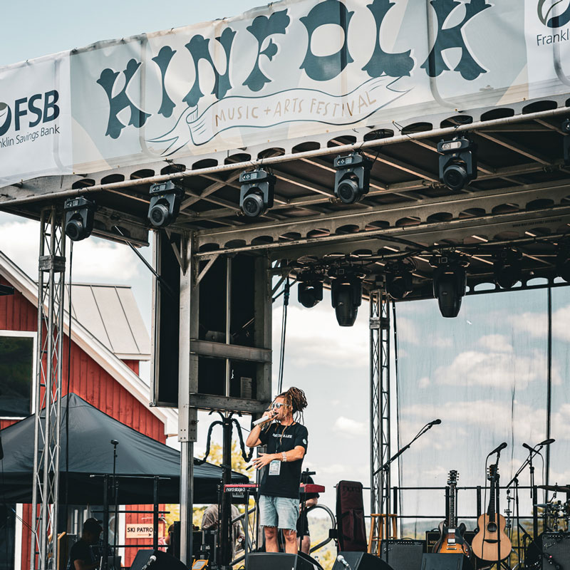 Singer with a microphone on the Kinfolk Music + Arts Festival stage on a sunny afternoon
