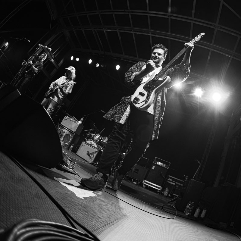 Black-and-white photo of a bassist singing into a microphone as his band plays