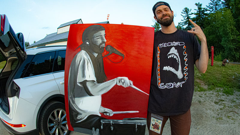 Smiling artist holding a painted portrait of a singer on a red canvas