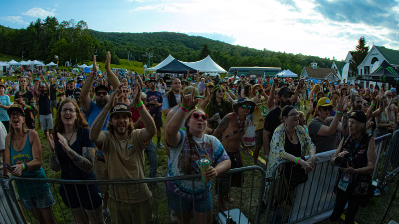 Cheering crowd with raised hands at the front barricade, with green hills behind