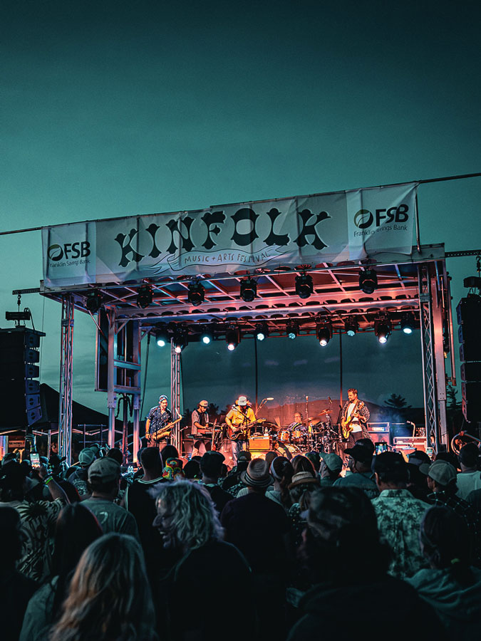 Band playing under the Kinfolk Music + Arts Festival banner at dusk while the crowd watches