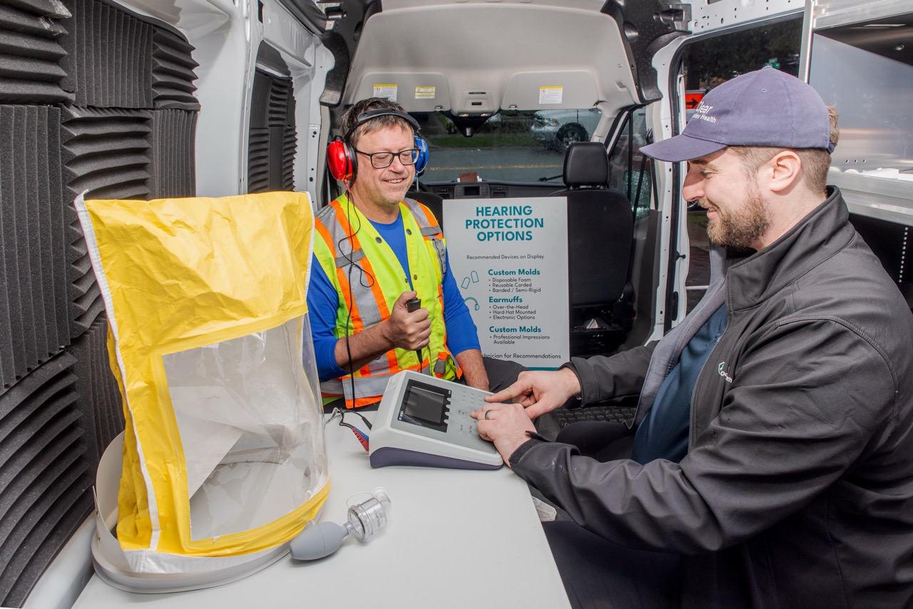 Worker in hearing test headphones while a Clear Work technician operates the audiometer in the van