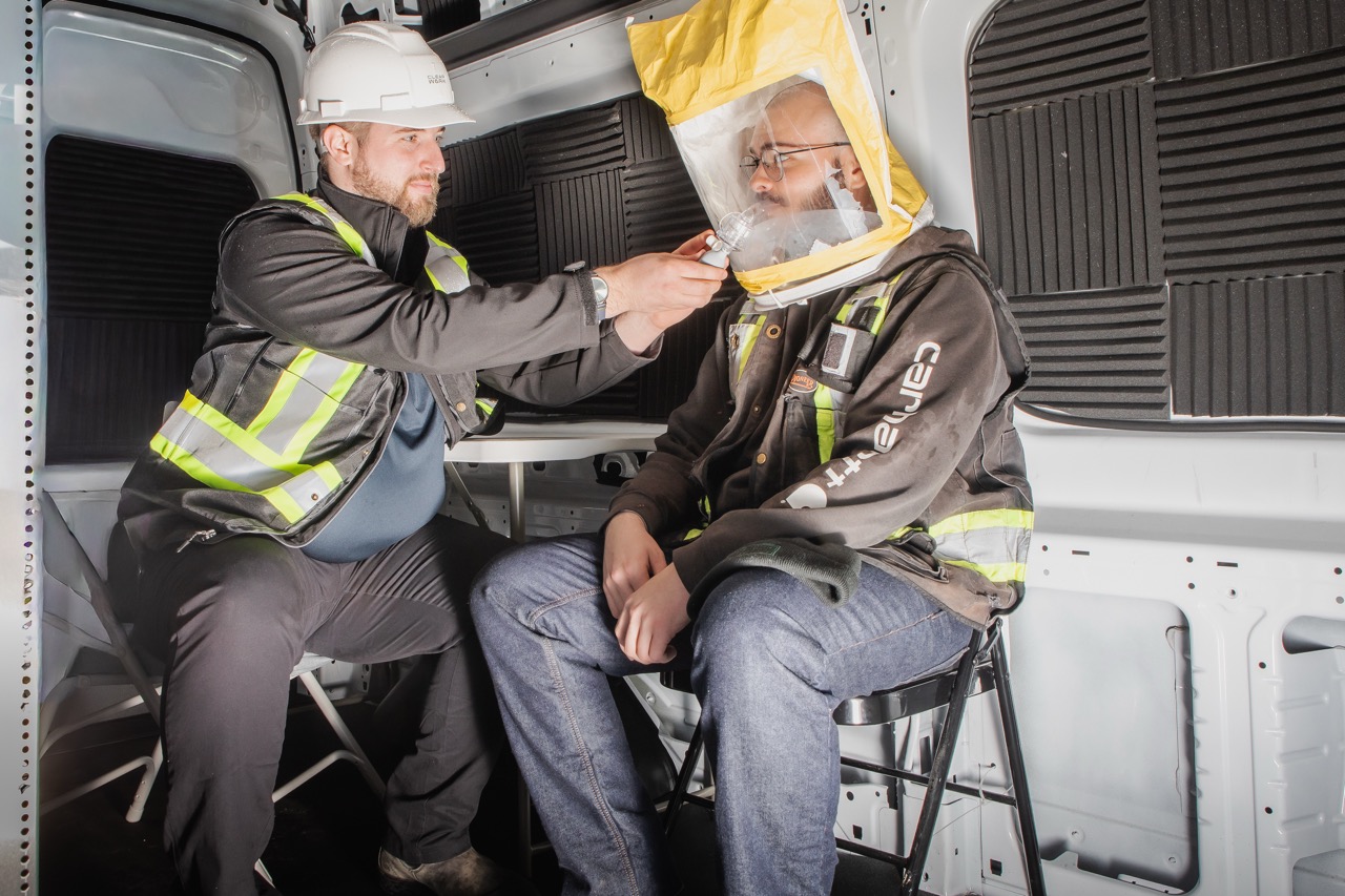 Clear Work technician performing a qualitative respirator fit test with a hood inside the mobile van