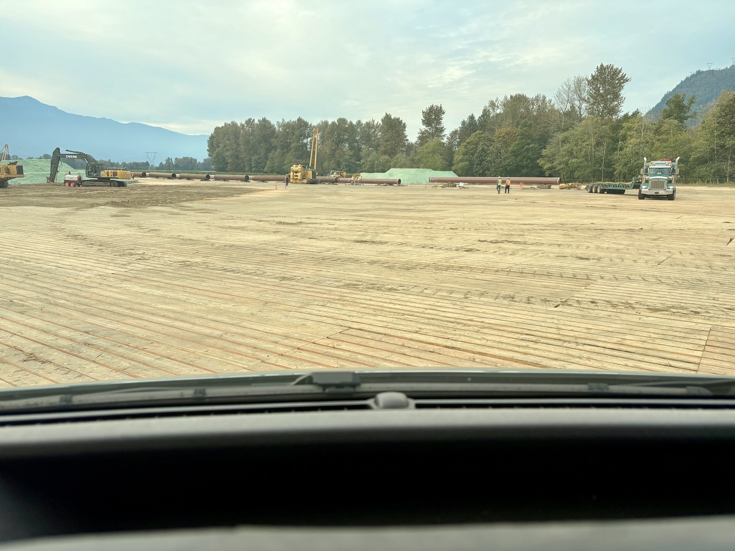 Pipeline construction site near Hope, British Columbia, with sections of pipe laid out on timber matting and crews working on site