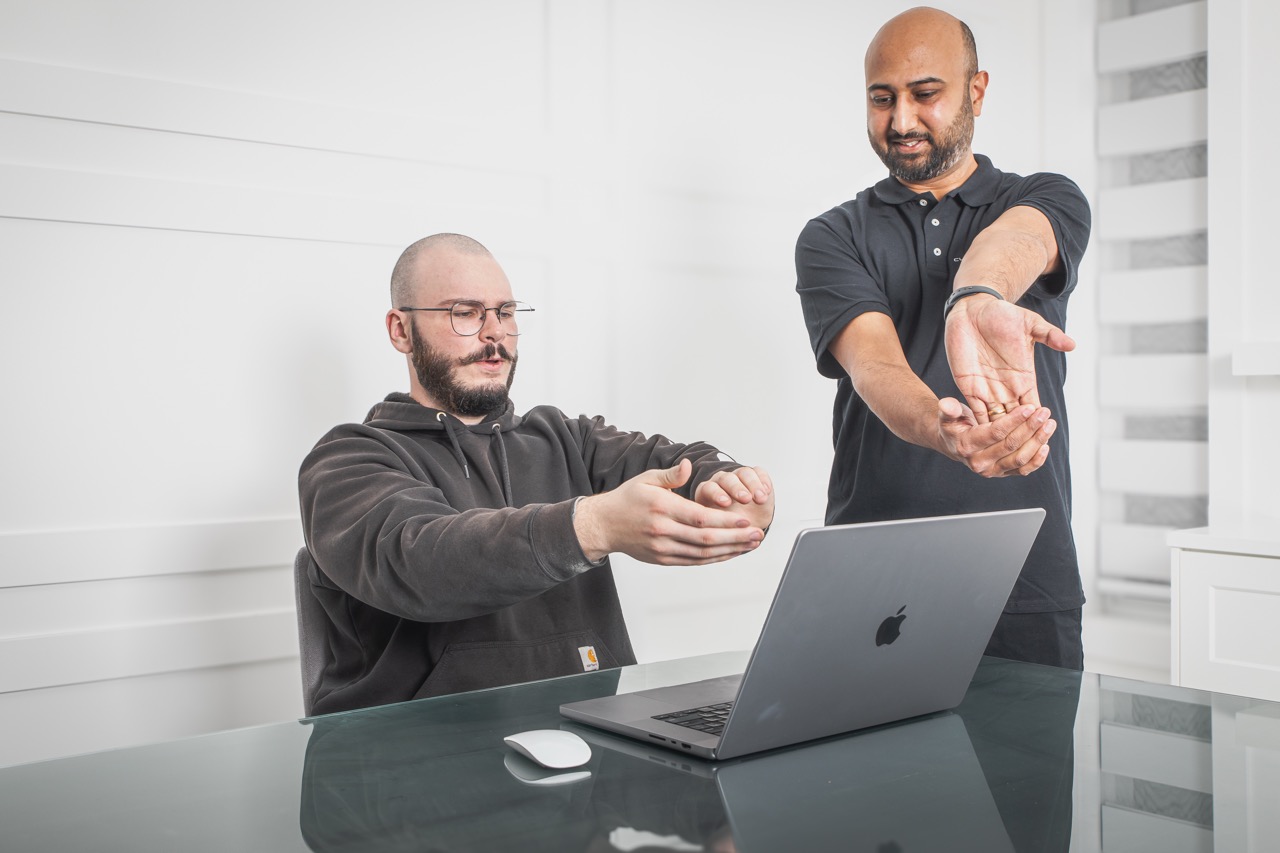 Ergonomic assessor demonstrating a forearm and wrist stretch to a seated worker at their desk
