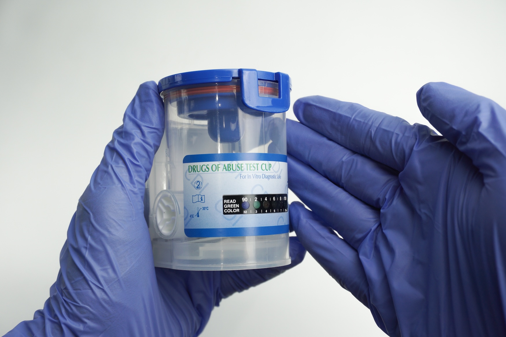 Gloved hands holding a sealed drugs of abuse test cup