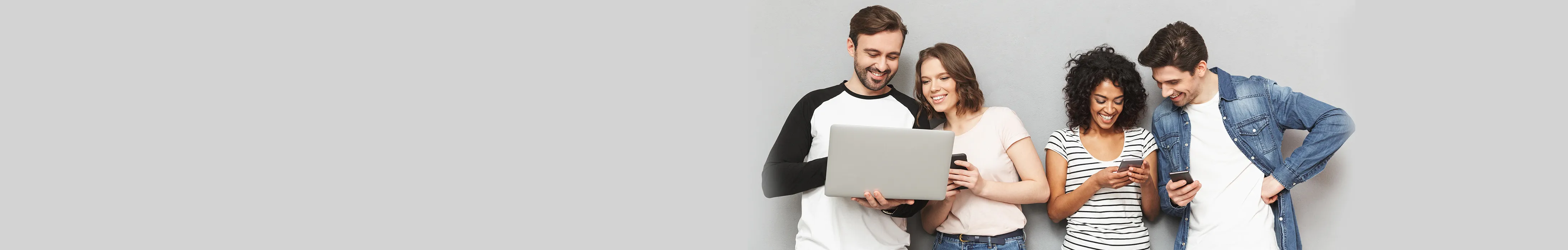 Four young adults standing close together, smiling and looking at a laptop and smartphones.