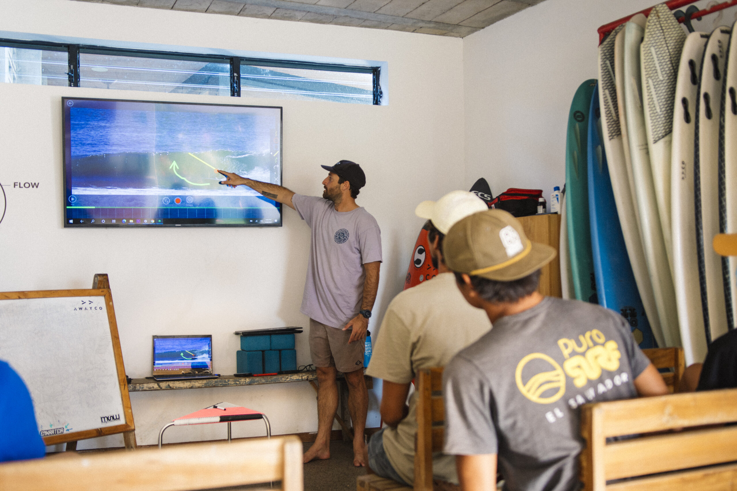 A coach reviewing surf session footage with students in the video analysis room at Puro Surf Academy